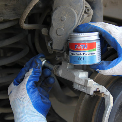 FOTU 661 brake caliper guide pin grease jar held by blue-gloved hands beside a dusty brake caliper and rotor