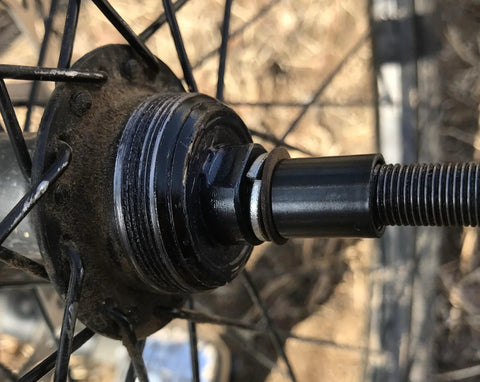 Bike wheel hub close-up showing threaded axle and locknut on black metal, with dirt