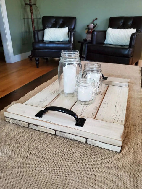 Rustic wooden tray with black handles, mason jar candles, and brown furniture in background.