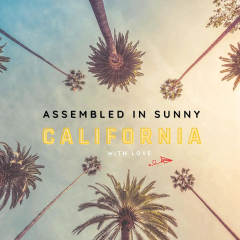 Palm trees with text 'Assembled in Sunny California With Love' viewed from below against a blue sky.