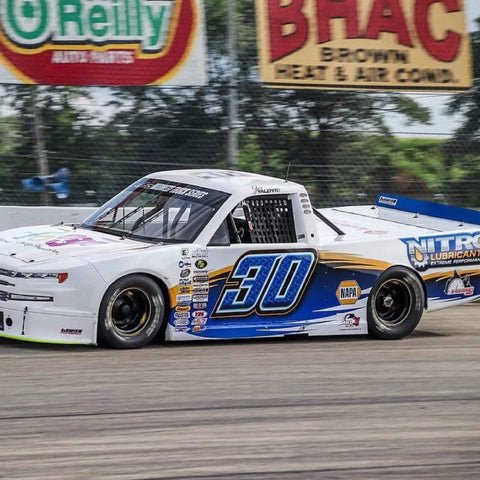 Race truck with Nitro Lubricants branding and number 30 on a track with sponsor banners in background