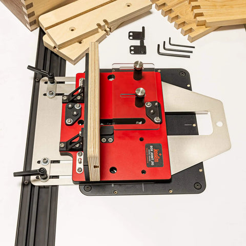 Pro Grade Box Joint Jig For Router Tables With Aluminum Indexing Keys And Smooth Bearing Glide System Includes One Quarter Inch, Three Eighths Inch, And One Half Inch Keys And Baltic Birch Fences For Precise Drawer And Box Joints, with visible red base and metallic components.