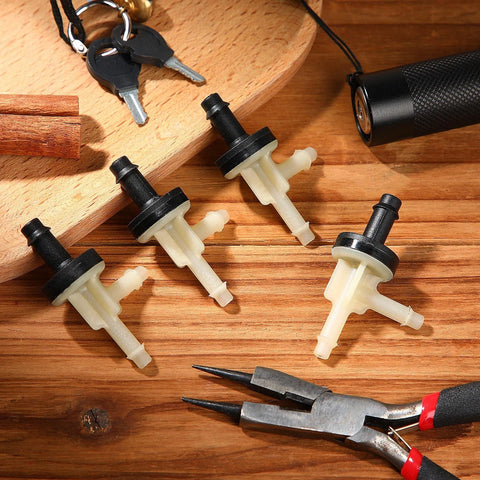 4 automotive vacuum check valves, beige plastic bodies with black tops, angled top view on wood with pliers nearby