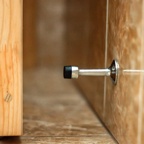 Wall-mounted metal door stopper with black rubber tip on tile floor