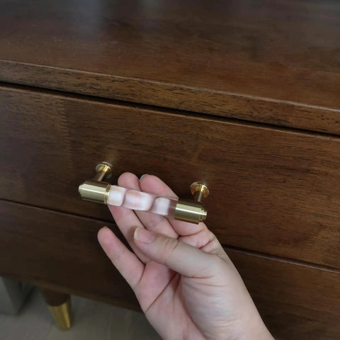 Hand holding brass and clear acrylic kitchen cabinet pull on dresser drawer.