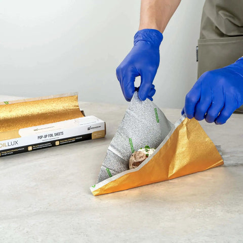 Person using Gold Embossed Pop-Up Foil Sheets 10.8 X 9 Inch interfolded greaseproof foil for wrapping food on counter.