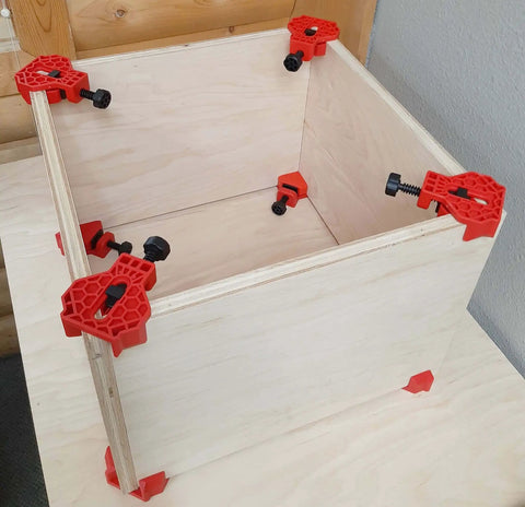 4 Pack Right Angle Corner Clamps For Cabinet Making And Box Assembly securing a wooden box at a 90 degree angle on a table