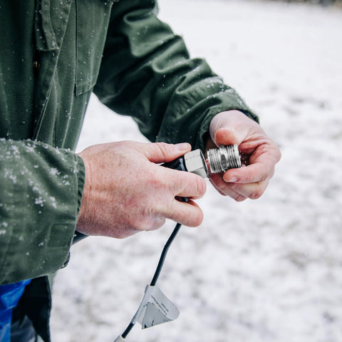 Heated RV water hose connector being assembled outdoors in a snowy setting with metal threaded fittings.
