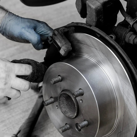 Automotive brake rotor with wheel hub and caliper, being worked on by blue-gloved hands.