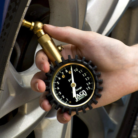 JACO Elite low-pressure tire gauge with brass body and black dial, 15 PSI, held to car tire valve.