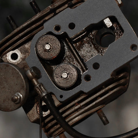 Automotive engine cylinder head with gray gasket plate, visible valve ports and oil grime on metal fins