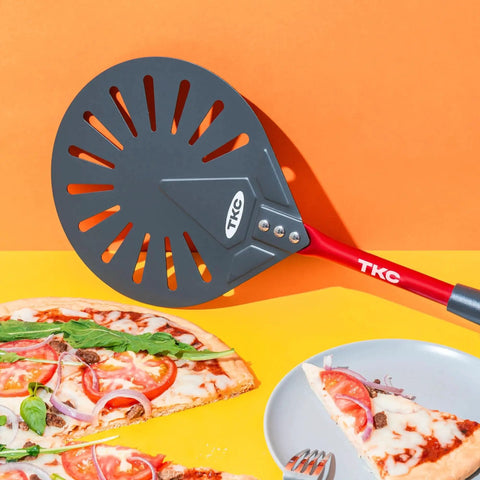 Pro Grade 9 Inch Perforated Pizza Peel With Extendable 27 To 41 Inch Handle For Indoor And Outdoor Ovens, Lightweight Aluminum Turning Peel, Nonstick Metal Pizza Turner Red TKC next to pizza