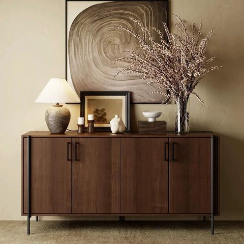 Wooden sideboard with modern decor, including a lamp, candles, and vase; features four cabinet doors with sleek handles.