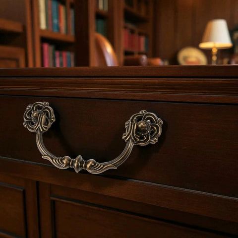 4-Pack Antique Brass Drawer Pulls 4.5 Inch Center-to-Center Drop Bail Dresser Handles Vintage Style Bronze Look Hardware for Cabinets Desks and Dressers 107mm Centers Zinc Alloy Construction Durable Ornate Finish installed on a wooden drawer in a classic study room.