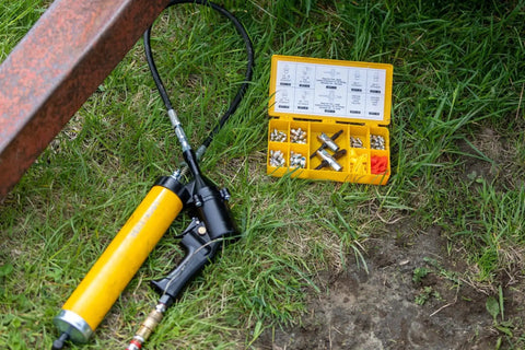 Complete Grease Fitting Replacement Kit With SAE And Metric Zerks For Straight And Ninety Degree Fittings Ten Each Of One Eighth NPT One Quarter Twenty Eight SAE LT Six By One Metric Eight By One Metric Includes Two Multi Tools And Twenty Caps LockNLube on grass with grease gun