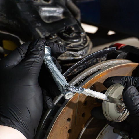 AGS Automotive Solutions 4oz SIL-Glyde silicone brake grease applied to brake caliper area with gloved hands.