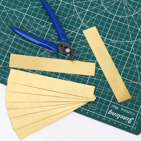 10 Piece Brass Shim Stock Set 6 Inch Long By 1 Inch Wide 0.002 Inch Thick Brass Strips on cutting mat with tool