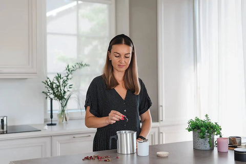 A woman using the Premium Soy Candle Making Kit Full Set With Soy Wax 7 Oz Jars And Tins, crafting candles at a kitchen counter.