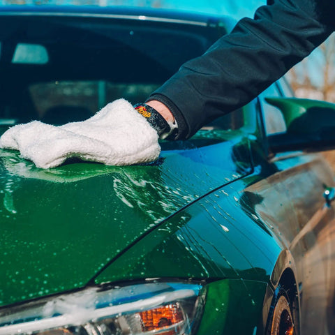 Person cleaning a green car hood with a white microfiber cloth using One Step Car Wash And Conditioner That Cleans And Conditions Without Stripping Wax And Foams Away Dirt And Road Grime While Preserving Wax Protection For A Dope Shine Meguiar's Gold Class 1.89L.