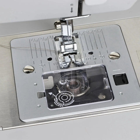 Front view of a silver bobbin cover plate installed over the bobbin housing on a sewing machine near the needle plate.