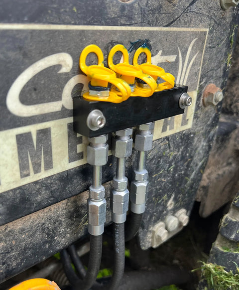 LockNLube grease fitting caps, yellow plastic caps on a metal mounting block with hydraulic hose fittings