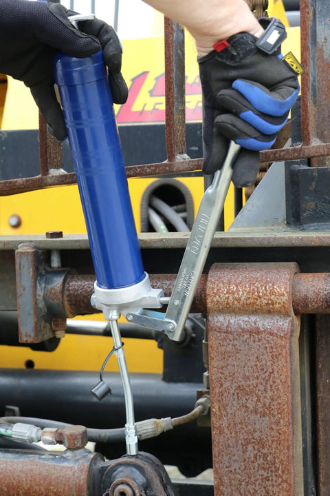 Lincoln blue lever-action grease gun attached to rusty industrial equipment with hose and coupler.