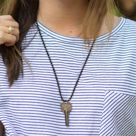 Woman wearing a bead chain necklace with a key pendant over a striped shirt.