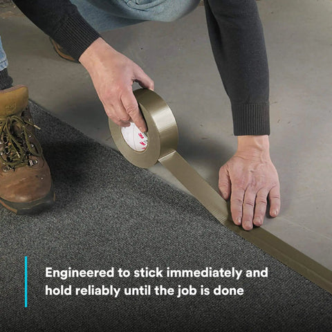Person applying Extra Heavy Duty Olive Duct Tape 6969 on carpet edge, demonstrating industrial strength and water-resistant bond