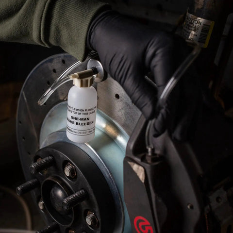 One-Man brake bleeder bottle with clear hose attached to car brake caliper near rotor