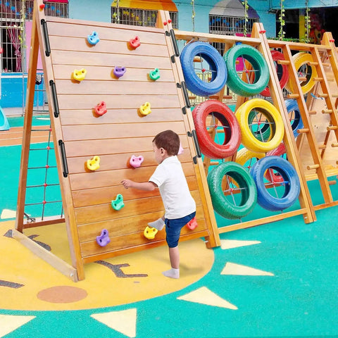 Child climbing a wooden frame with colorful grips, next to a tire-based climbing structure on an outdoor playground.