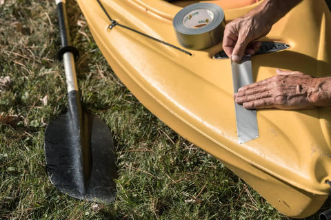 Applying Duct Tape 1.88 Inch By 60 Yard Silver For Quick Repairs And Sealing on yellow kayak beside black paddle on grass