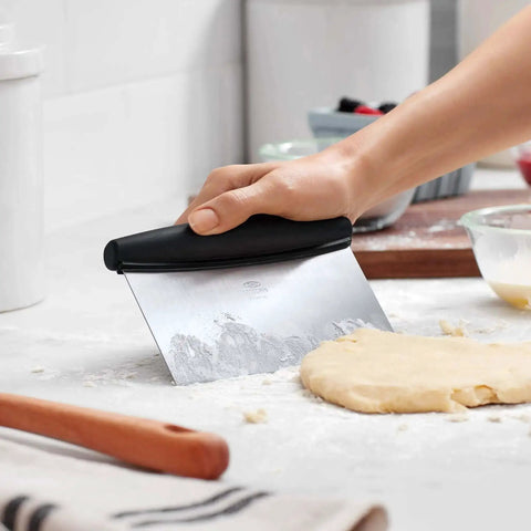 Hand using Stainless Steel All Purpose Scraper and Dough Cutter for Pizza Bread and Cookie Dough, Vegetable Chopper with Built In Quarter Inch Markings, Dishwasher Safe Kitchen Essential for Precise Prep on dough.