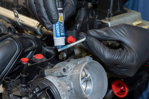 Blue Medium Strength Threadlocker Stick With Self Feeding Applicator, 9 Grams being applied to a metal thread in an engine