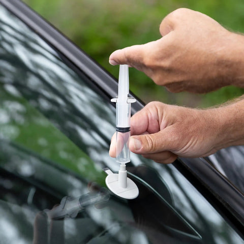 Close-up of hands using the Windshield Chip Repair Kit For Stone Damage And Bullseyes, filling a chip on a car windshield.