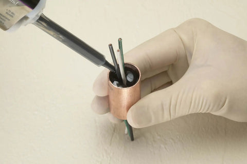 Applying 3M Scotch-Weld Clear Epoxy Adhesive DP100 Plus to wires in a copper fitting, showcasing reliable bonding application.