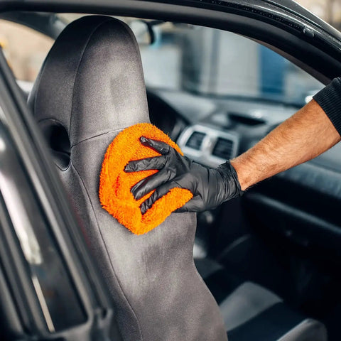 Person cleaning car seat with orange cloth, wearing Black Nitrile Exam Gloves Medium 4 Mil Powder Free Latex Free Food Safe Medical Grade Puncture Resistant.