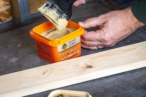 All Purpose Wood Filler Natural Finish 16 Oz Water Resistant Indoor Outdoor Use in orange tub with person applying filler to wood.