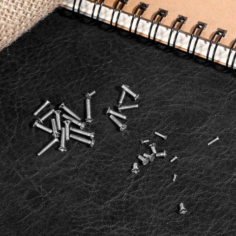Scattered black carbon steel screws from 500 Pcs Tiny Replacement Screws Kit For Glasses Watches Laptops Hard Drives And SSDs.
