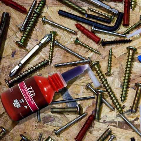Purple Threadlocker High Strength Oil Resistant Anaerobic Adhesive bottle surrounded by various screws on a workbench