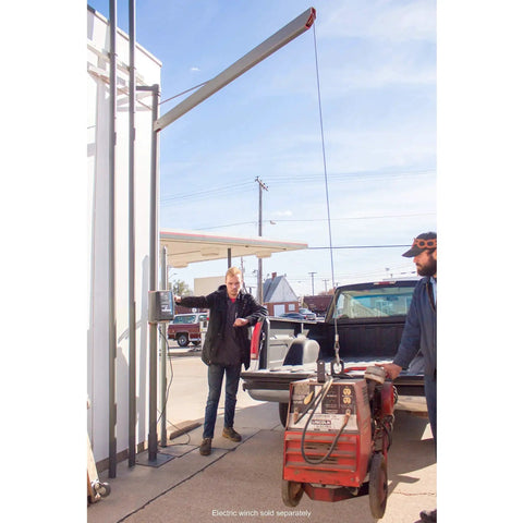 Blue winch cable with hook attached to a tall outdoor hoist beside a pickup truck.