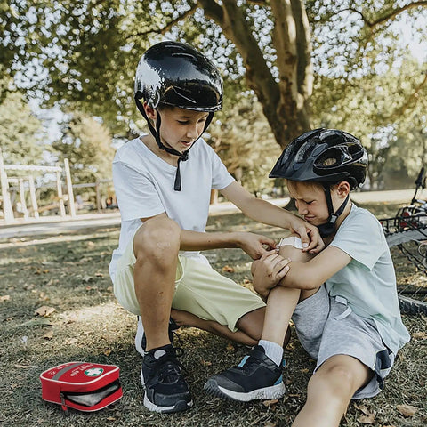 Two children with helmets using 130 Piece All-in-One First Aid Kit With Hospital Grade Medical Supplies outdoors in a park.