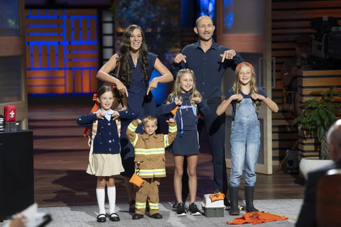 Group of people on stage with children wearing costumes, showcasing Versatile Triangular First Aid Bandage For Splints And Sprains 36.6 X 36.6 X 53.9 Inch Cotton Triangle For Arm Sling Wound Dressing Head Bandage Cravat And Limb Support Warrior Kid Medic As Seen On Shark Tank.