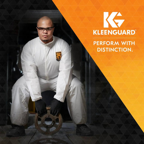 Man wearing Kleenguard coveralls and polarized safety glasses with smoke lenses, holding a metal fitting in an industrial setting.