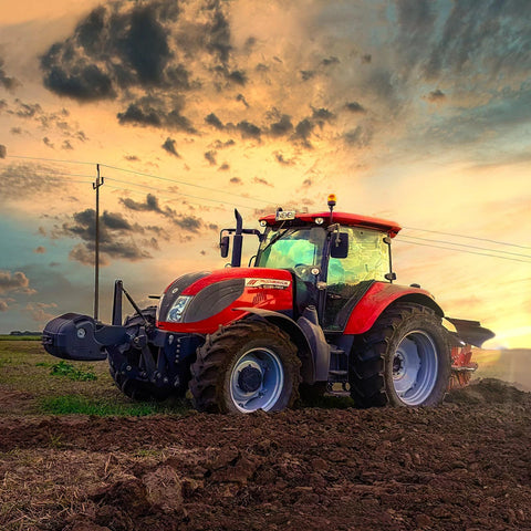 Red McCormick tractor in a plowed field at sunset with large rear tires.