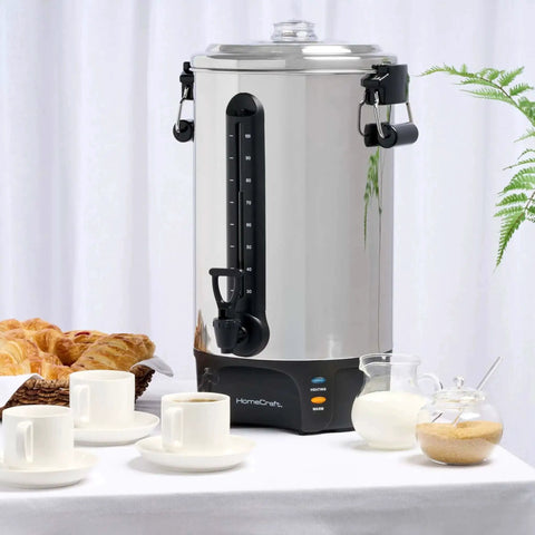 100 Cup Coffee Urn And Hot Beverage Dispenser With Dripless Faucet, stainless steel on a table with pastries and cups, side view