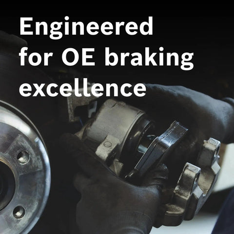 Front ceramic brake pad set installed on a brake rotor with caliper; gloved hands.