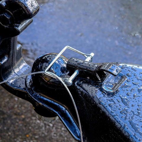 Pack Of Ten Heavy Duty Trailer Pins Two And Three Quarter Inch Long By One Quarter Inch Wide With PTO Pins Lock Pins Trailer Hitch Pins And Shaft Locking Coupler Pins For Farm Trailers Towing Lawn Equipment And Hitches installed on a damp black hitch coupler.