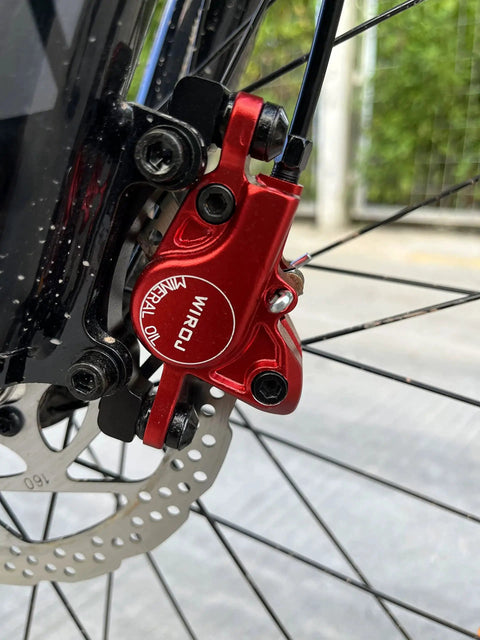 Red WIROJ hydraulic disc brake caliper, side view, mounted on front MTB fork with drilled rotor