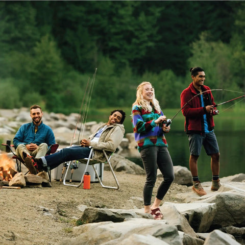 Group of people fishing at a lakeside with camping gear, holding Zebco Bullet Spincast Fishing Reel, joyful and relaxed.