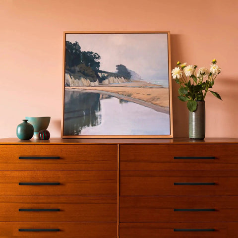 Painting of coastal landscape on dresser with vases and flowers